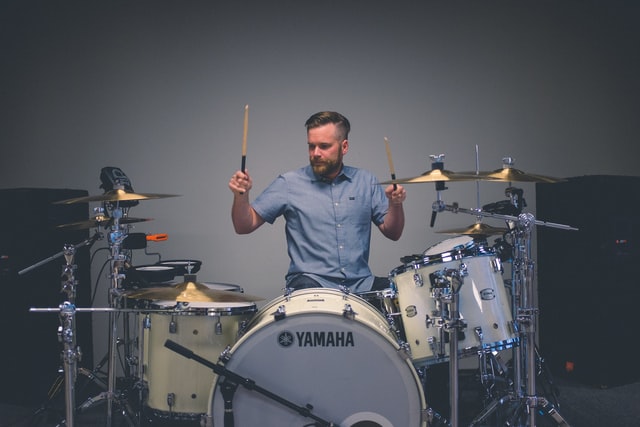 A man playing the drums, with large speakers next to him