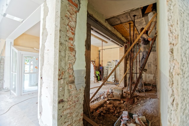 A man on the ladder in the corner of a room in an apartment that's being renovated.