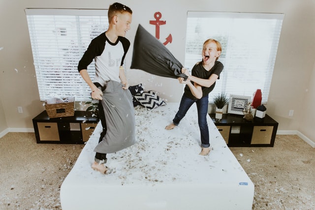 A boy and a girl jumping on the bed and having a pillow fight in their child-friendly home