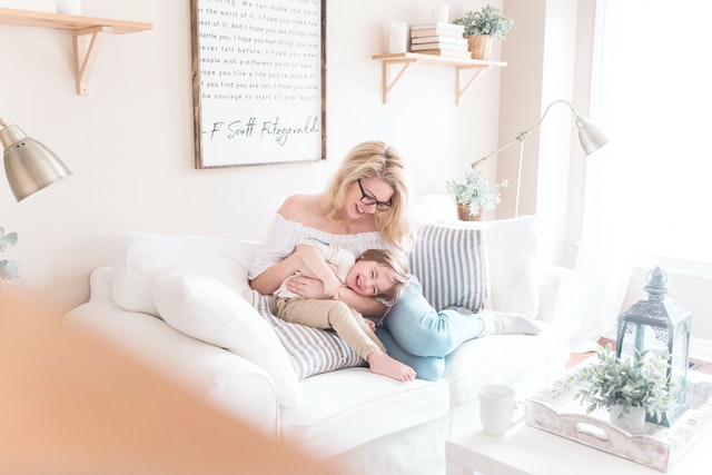 Woman holding her child and cuddling on a sofa bed in a light living room, representing how to make your home more child-friendly