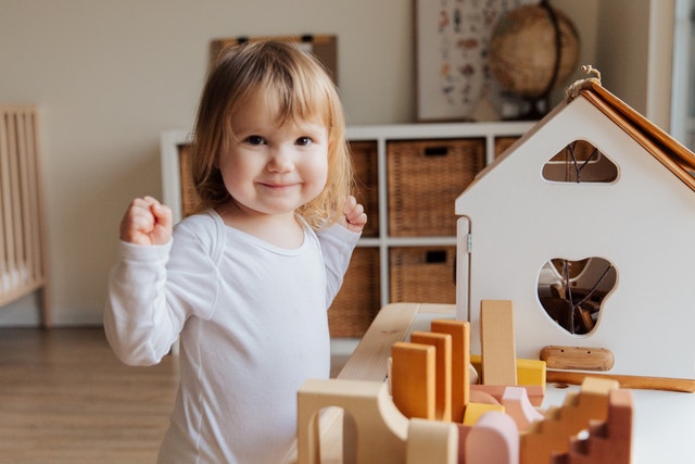Little girl in white blouse playing with a dollhouse in her room