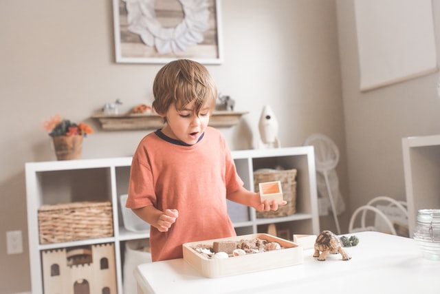 Boy in an orange sweater playing with toys on a table in his playroom