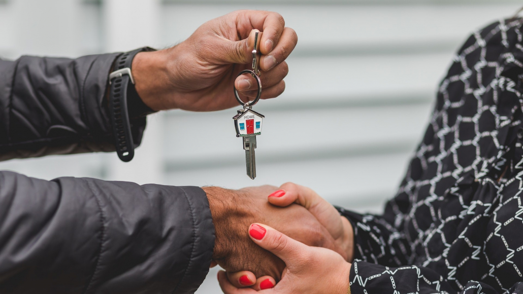 A man hands a woman the keys to a house after a successful sale