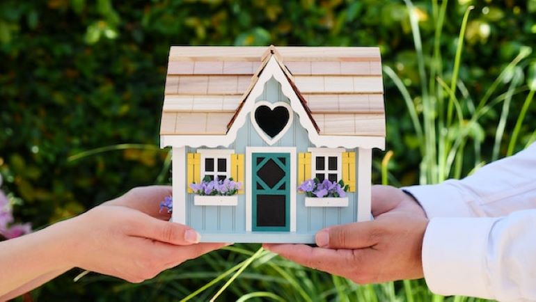 Two people are holding a model of a wooden house