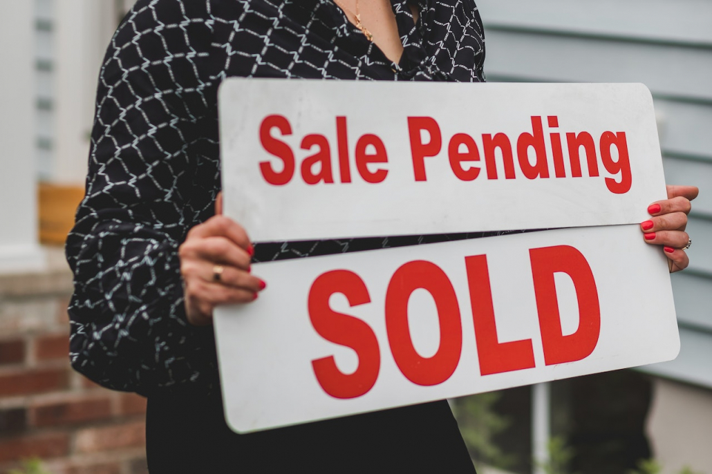 A person holding a sign with red letters spelling “sale pending” and “sold.”