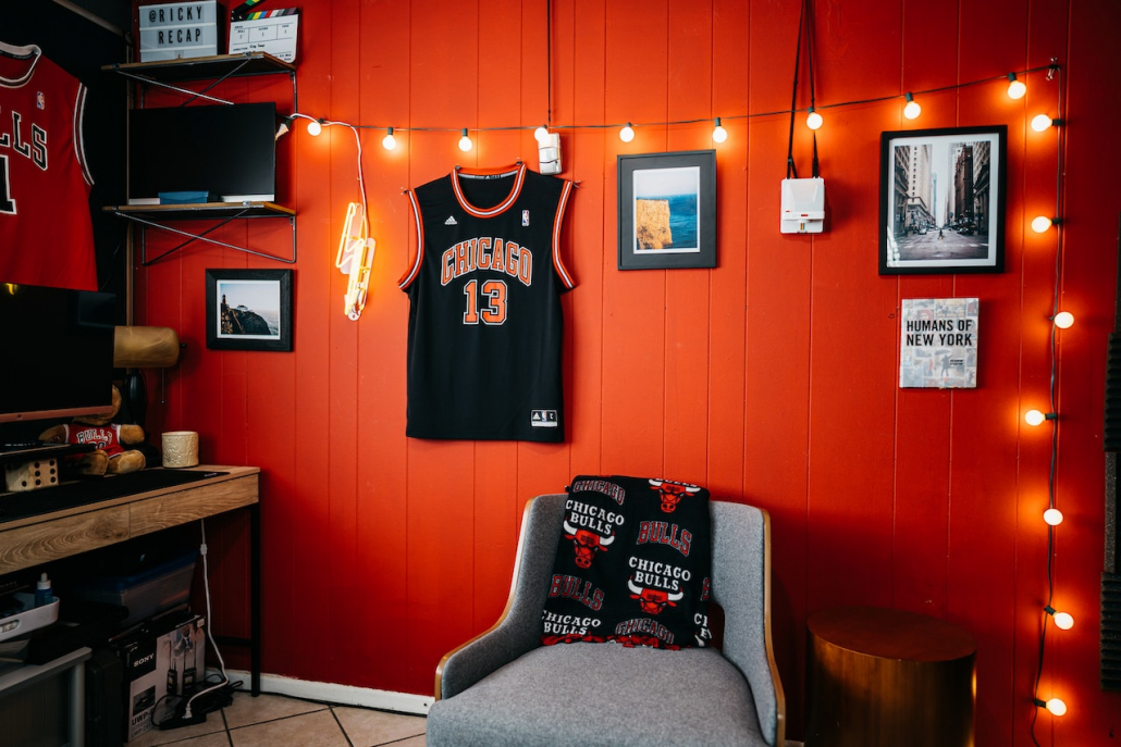 A room with a red wall and a basketball team shirt, and other personal items on the wall.