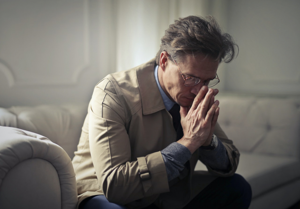 A man that looks like he is a bit sad, sitting on the sofa.