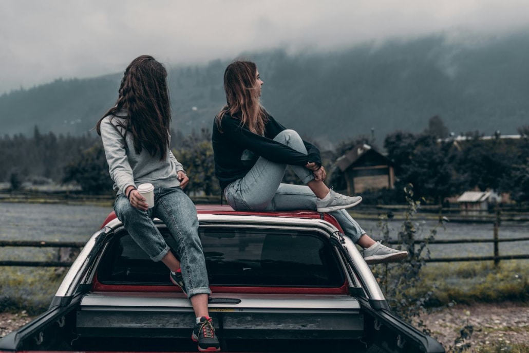 Two women sitting on the roof of their vehicle and enjoying the view.
