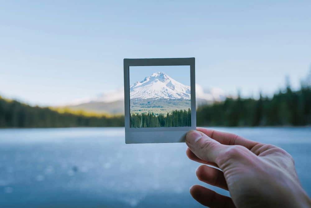 A person holding a polaroid picture of a snow-covered mountain