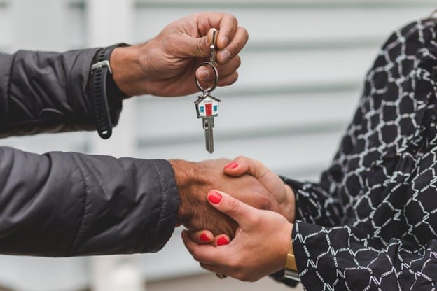 A man giving a key to a lady while shaking her hand