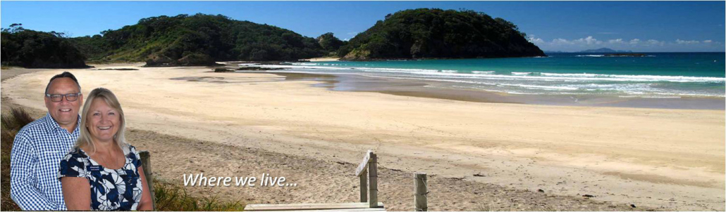Smiling couple on a sunny beach with turquoise water and green hills in the background; overlay text reads'Where we live…'